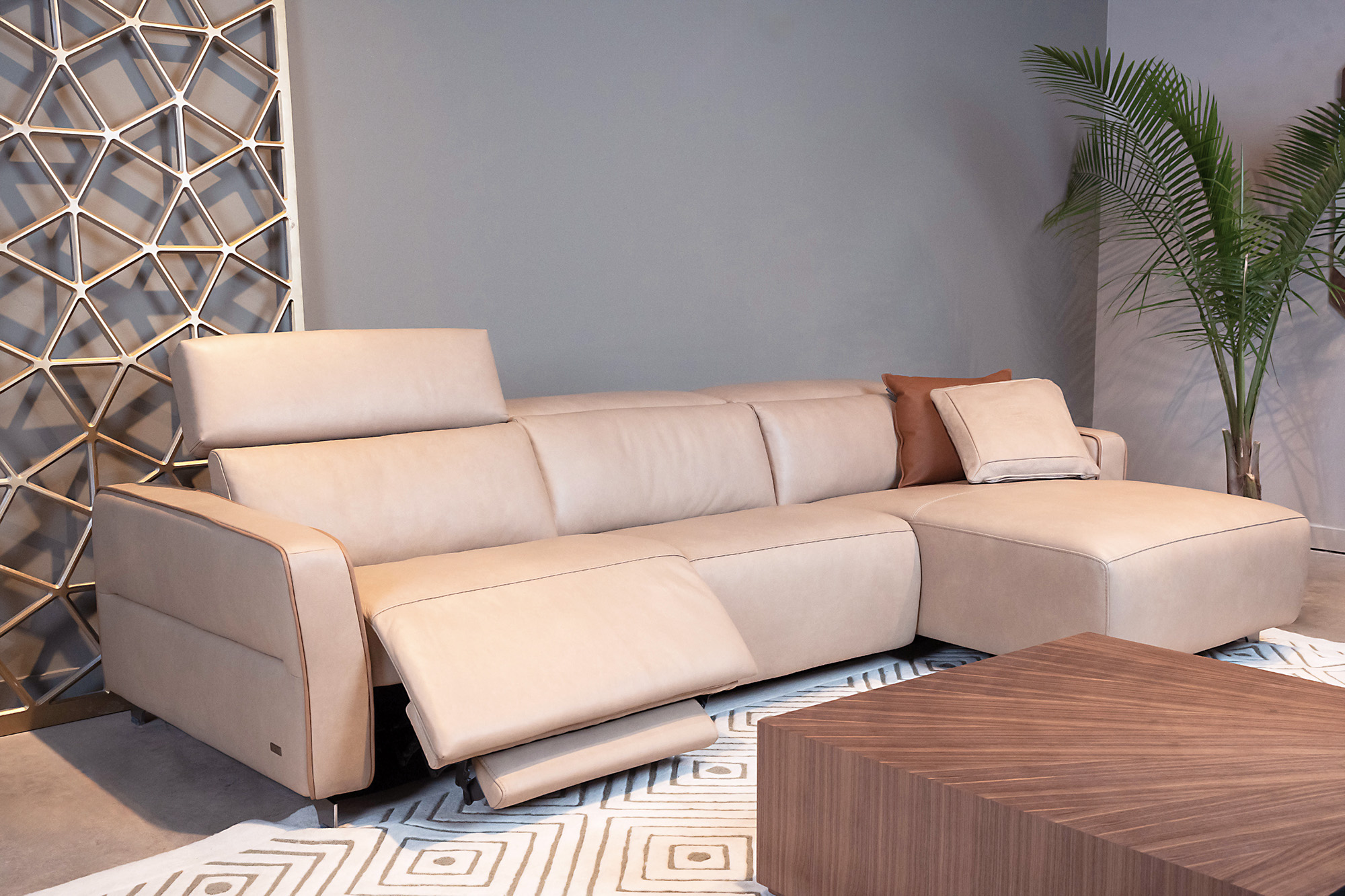 A picture of a tan leather sectional sofa in a modern living room, with the nearest seat reclined back and its footrest extended